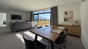 A modern living room with a sofa, TV, dining table, chairs, and a large window with a view.