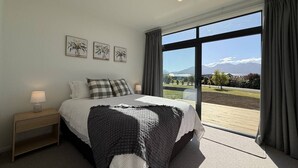 A bedroom with a bed, a bedside table, and a view of the outdoors.