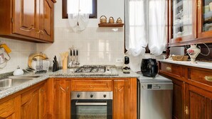 Cozinha com armários de madeira, fogão a gás, lava-louças e janela com cortina.