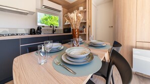 A modern kitchen with a dining area, wooden cabinets, a built-in microwave, and a window with a view of greenery.