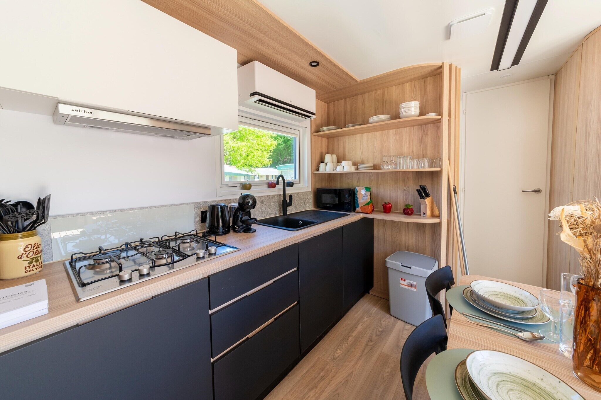 A modern kitchen with a gas stove, sink, and wooden shelves.
