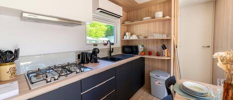 A modern kitchen with a gas stove, sink, and wooden shelves.