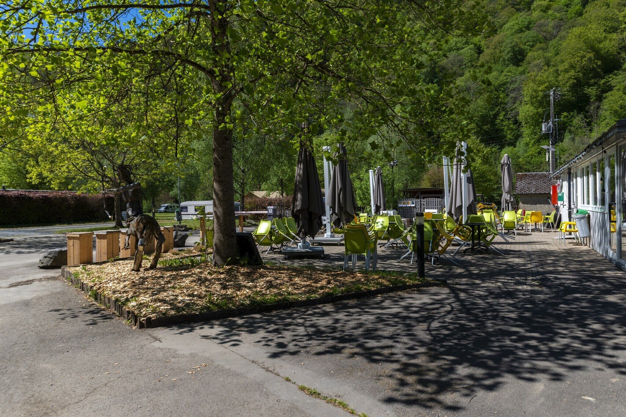 A park with outdoor seating, trees, and a building with a tiled roof.