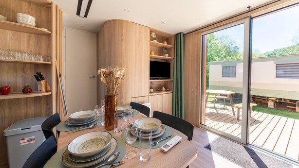A dining area with a table set for four, a wooden cabinet with shelves, and a sliding glass door to an outdoor deck.