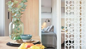 A room with a wooden table, a glass vase with greenery, a bowl, and a bed with a grey bedspread. - Mobile home Keiheuvel (6p) (Balen)