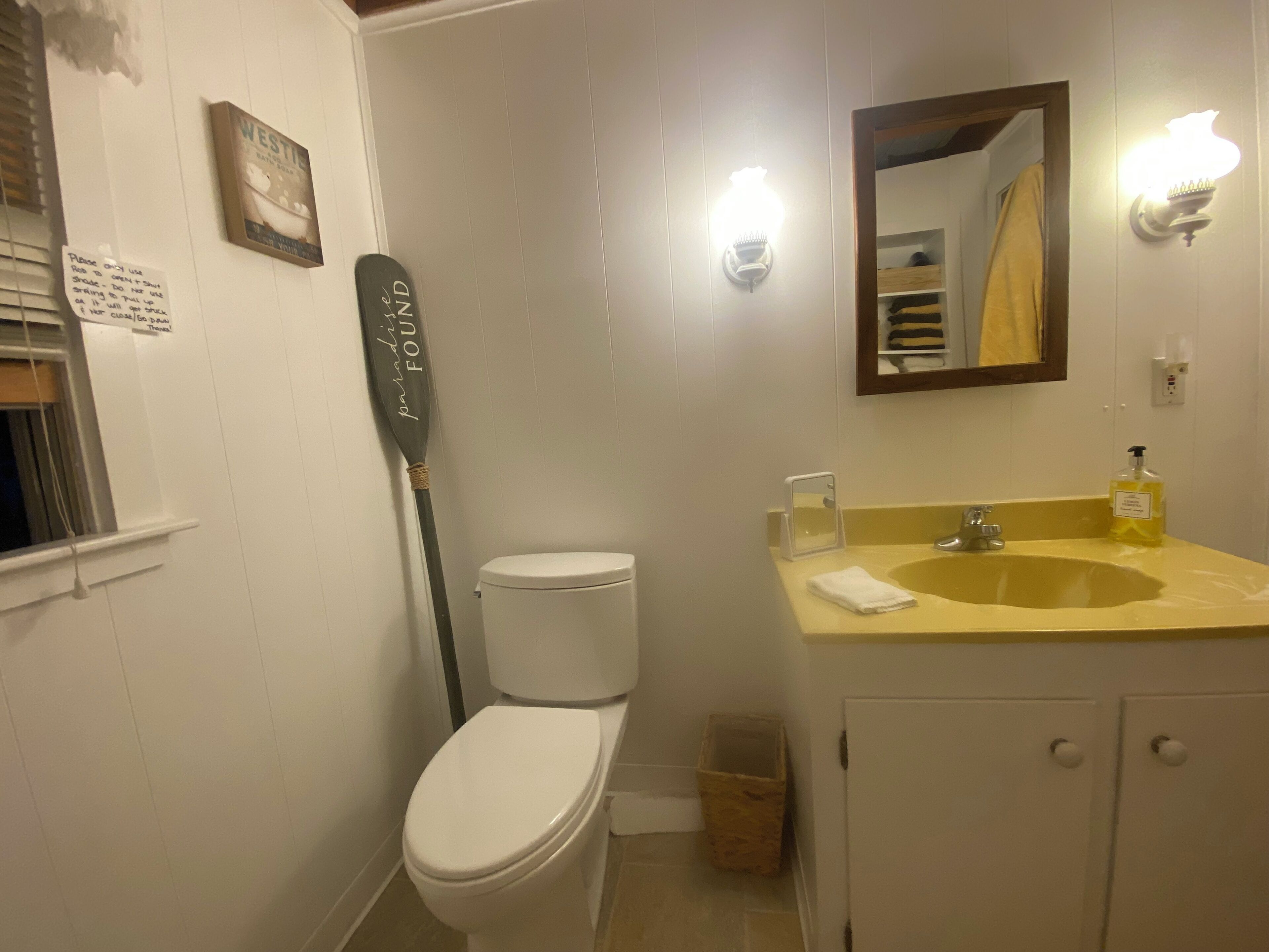 Une salle de bain avec des toilettes, un lavabo, un miroir et une planche de paddle qui est appuyée contre le mur.