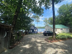 A residential area with a gravel driveway, a blue house, a green-roofed house, and a parked car. - Charming Great East Lake 4 Season Waterfront Home! (Acton)