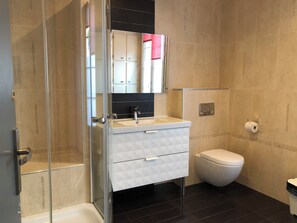 A modern bathroom with a glass shower enclosure, a white sink with a black countertop, a toilet, and a wall-mounted toilet paper holder. - Beautiful duplex apartment for 5 people, 5 minutes from the IGR Metro Station 14, 10 minutes from Paris (Villejuif)