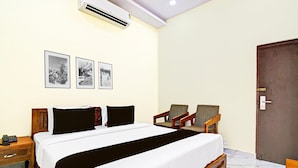 A hotel room with a bed, two armchairs, a wooden nightstand, and three framed pictures on the wall. - Blissful Stays at Dwarakanagar Near Gurudwara (Visakhapatnam)