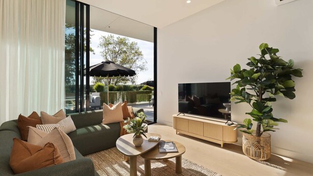 A modern living room with a sofa, coffee table, TV, and a large window overlooking a garden.