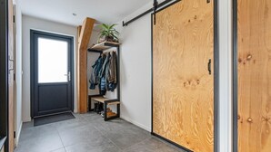 Un couloir avec une porte coulissante en bois, un banc, un porte-chaussures et un portant à vêtements avec des articles suspendus.