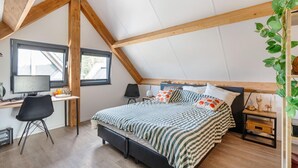 Une chambre avec un plafond en pente, un lit avec une literie à rayures, un bureau avec un ordinateur et une fenêtre.