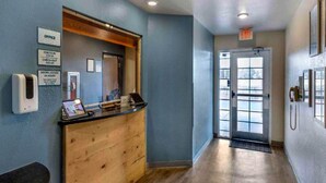 A reception desk with a wooden counter, a sign indicating office hours, and a glass door leading outside. - 2 Full Beds | Non-Smoking, Kitchen (Bossier City)