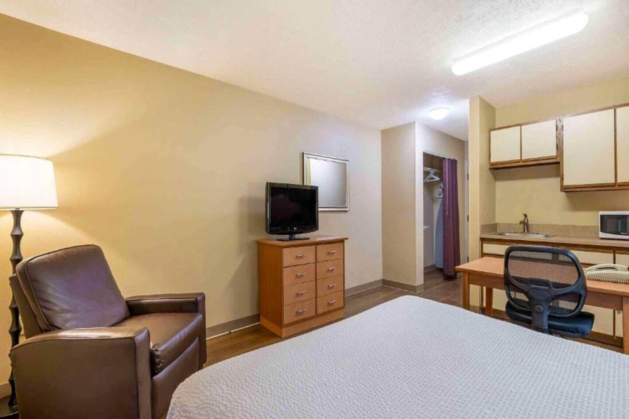 Une chambre d’hôtel avec un lit, un bureau et une chaise, un téléviseur posé sur une commode, et une salle de bain visible à travers une porte ouverte.