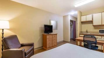 Une chambre d’hôtel avec un lit, un bureau et une chaise, un téléviseur posé sur une commode, et une salle de bain visible à travers une porte ouverte.
