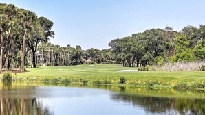 Golfkenttä, jonka edustalla on lampi, ja jota ympäröivät puut ja kirkas taivas.