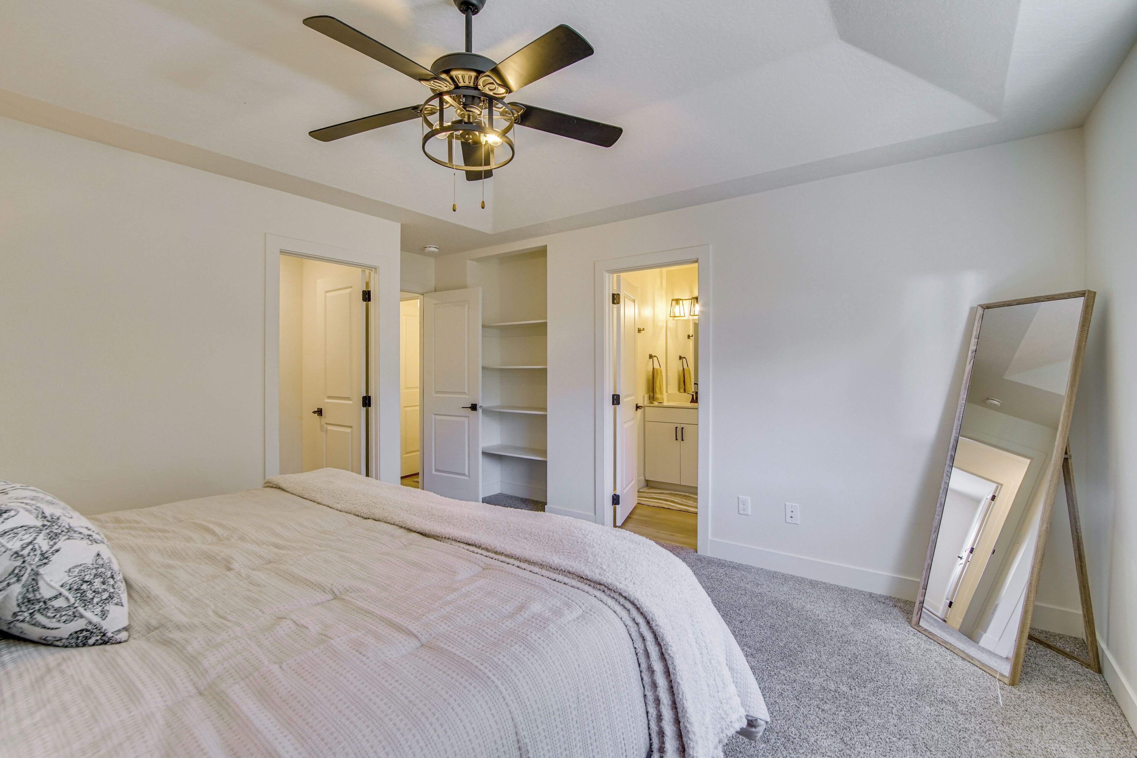 Un dormitorio con cama, ventilador de techo, espejo y vestidor.