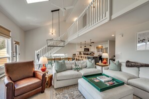 A spacious living area with a high ceiling, a staircase, and a kitchen in the background. - White Mtn Adventure Hub! Group Escape w/ Views (Jefferson)