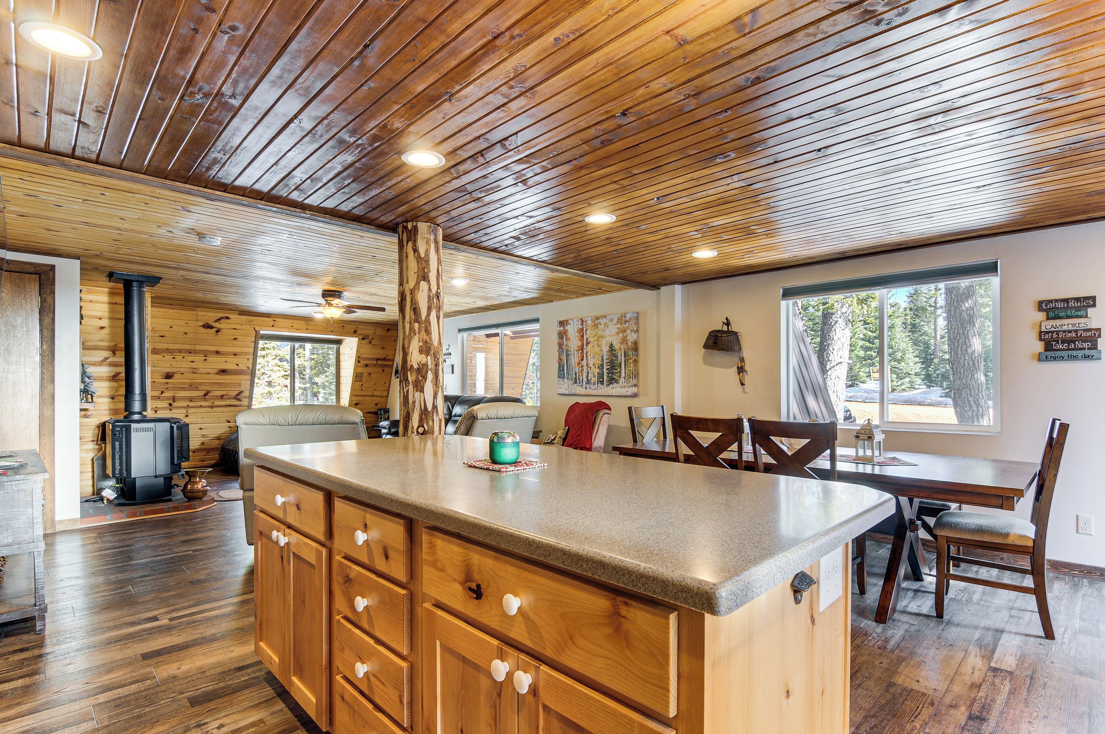A wooden interior with a central island, wooden cabinets, a dining table, and a view of trees through a window.