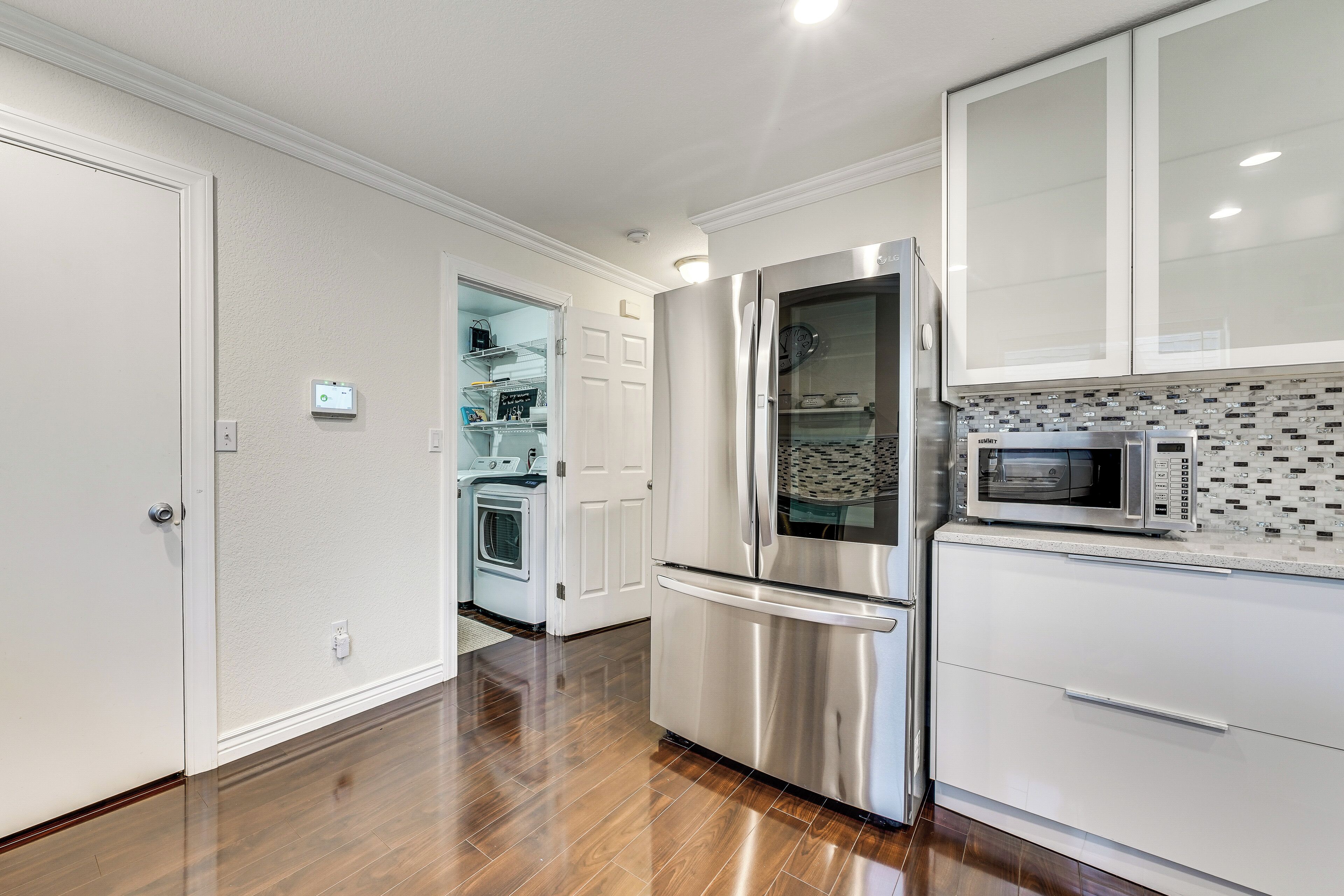 A modern kitchen with stainless steel appliances, white cabinetry, and a patterned backsplash.