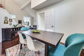 Een eetgedeelte met een donker houten tafel, witte stoelen en een kleurrijk vloerkleed.