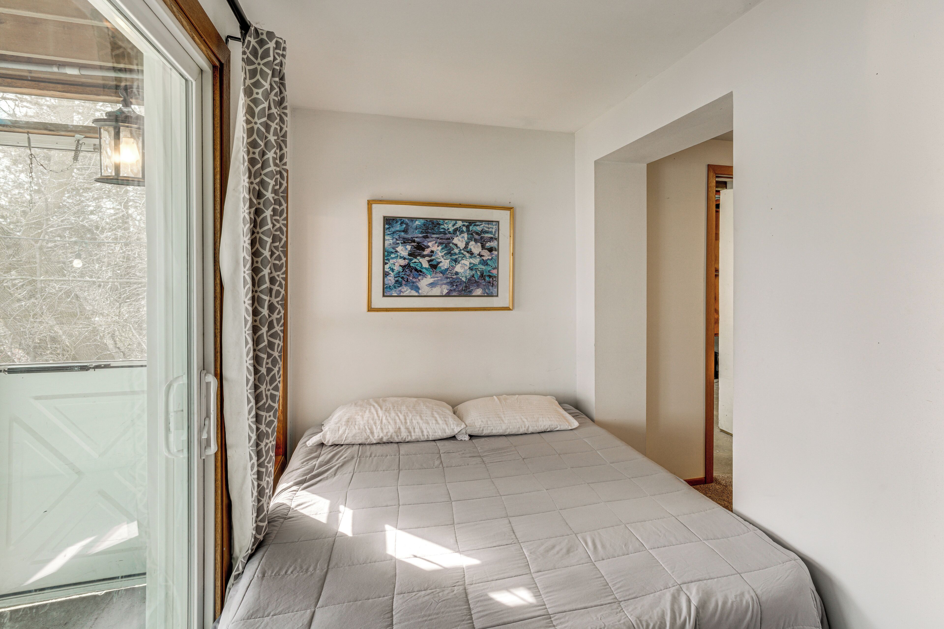 A bedroom with a bed, a framed picture on the wall, and a door leading to another room.