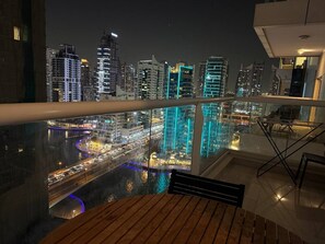 A balcony with a view of a cityscape at night, including illuminated buildings and a river. - Beach Lux New 2BD | Marina view | CEG Group (Dubai)