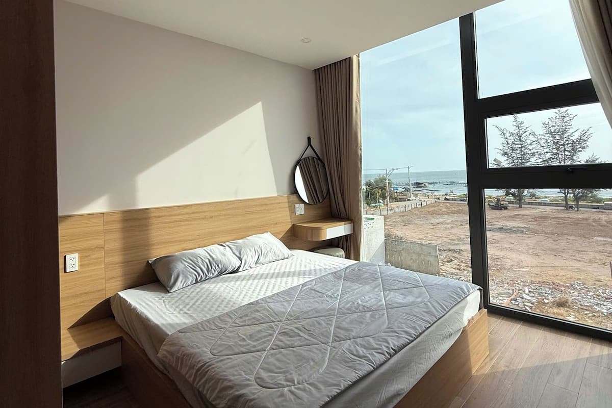 Un dormitorio moderno con una cama grande, cabecera de madera, mesita de noche, una silla colgante y vistas al exterior.