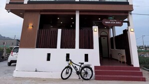 A multi-story building with a balcony, a bicycle parked in front, and a sign indicating 'Homestay NHA CUA DAU.'