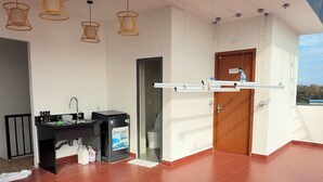A spacious balcony with a red-tiled floor, a black kitchen area with a sink, and a wooden door.