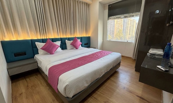A modern hotel room with a large bed, a nightstand, a desk, and a window with a view of buildings.
