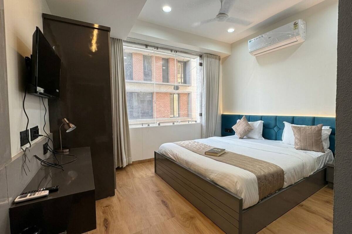 Quarto de hotel com cama, televisão, escrivaninha, janela e ar condicionado.