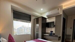 A hotel room with a bed, a window, a kitchenette, and an air conditioning unit. - Hotel Rajvanshi Inn (Ahmedabad)
