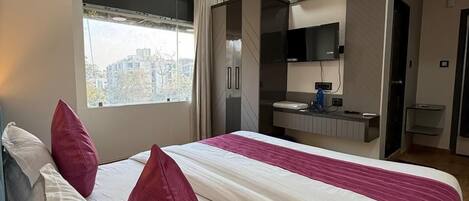 A hotel room with a bed, a window, a kitchenette, and an air conditioning unit.