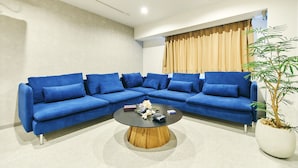 A modern living room with a blue sectional sofa, a round coffee table, and a potted plant.