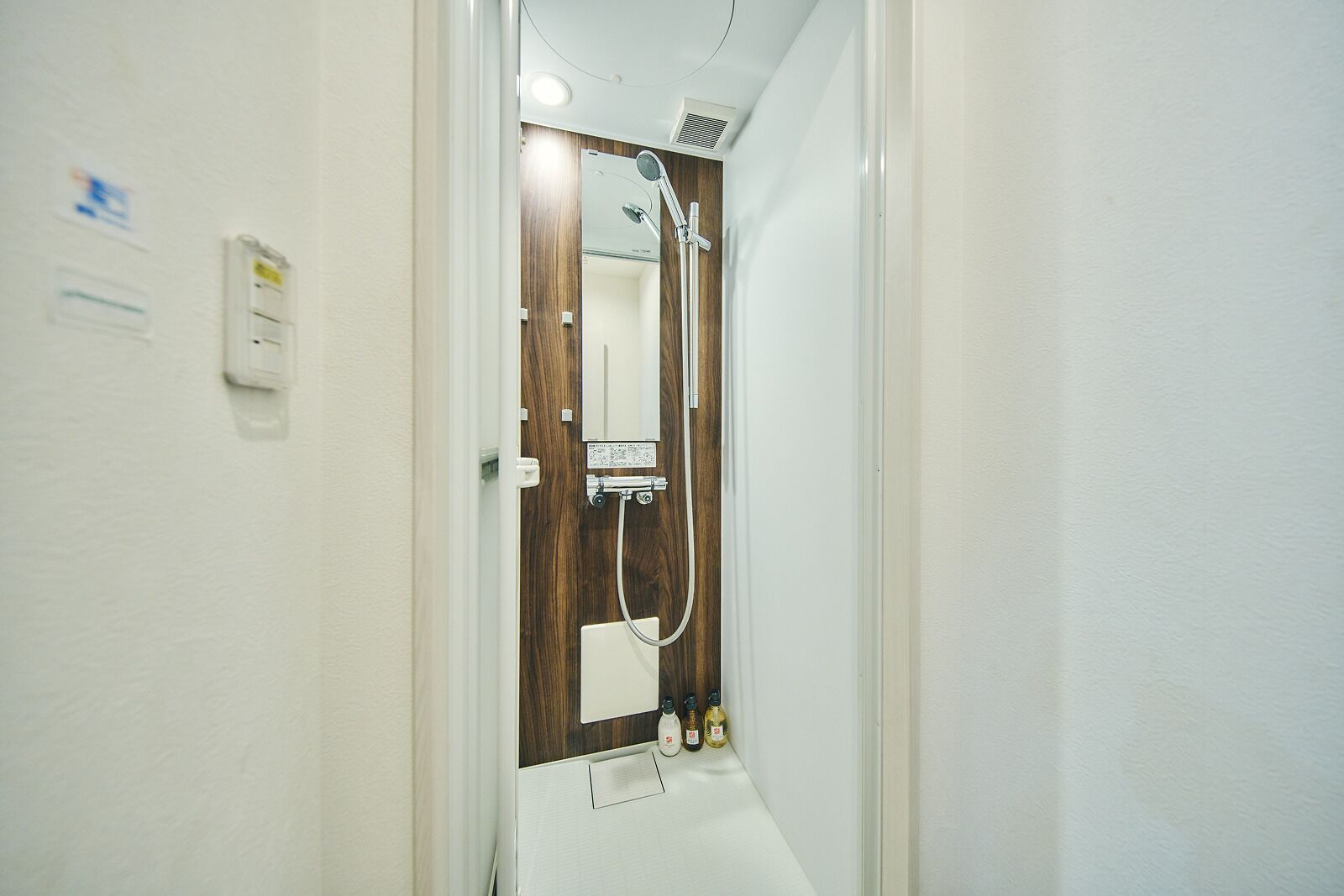 A narrow hallway leading to a bathroom with a shower, a mirror, and a wall-mounted heater.