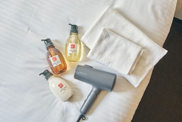 A bed with white linens, a white towel, and three bottles of body care products. - &AND HOSTEL NAMBA SOUTH (Osaka)