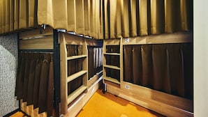 A room with wooden bunk beds, each with a shelf and a hanging curtain.