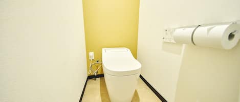 A small, narrow bathroom with a toilet, a toilet paper holder, and a visible electrical outlet.