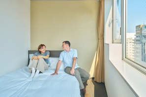 Una habitación de hotel con cama, ventana con cortinas y vista a edificios.