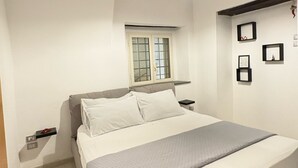 A bedroom with a bed, a window with blinds, a hanging light fixture, and a wall-mounted shelf with framed pictures. - Domus Gazzara, cozy and comfortable vacation home in the heart of the historic center (Napoli)