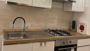 A kitchen with white cabinets, a stainless steel sink, a gas stove, and an oven. - Domus Gazzara, cozy and comfortable vacation home in the heart of the historic center (Napoli)
