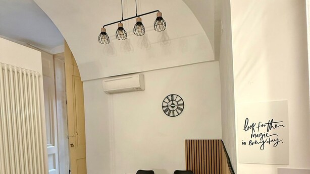 A modern dining area with a wooden table, black chairs, a wall clock, and a ceiling light fixture. - Domus Gazzara, cozy and comfortable vacation home in the heart of the historic center (Napoli)