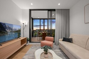 Ein modernes Wohnzimmer mit Flachbildfernseher, einer Couch, einem Couchtisch mit Pflanze und einem Balkon mit Essbereich.
