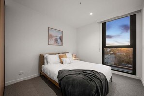 Ein Schlafzimmer mit großem Fenster, einem Bett, einem Nachttisch und einem Wandbild.