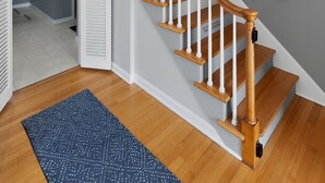 A staircase with wooden steps and white railings, a blue patterned rug on the floor, and a wall-mounted light fixture. - Irish Safari Retreat / Walk to Zoo / Minutes to Notre Dame (South Bend)