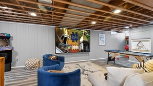 A room with a pool table, blue and white furniture, a large TV, and a gaming console. - Irish Safari Retreat / Walk to Zoo / Minutes to Notre Dame (South Bend)