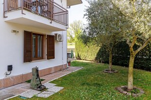Un edificio bianco con un balcone, un albero e un prato curato.