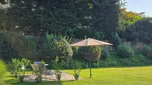 Un espace extérieur verdoyant avec une table et des chaises de patio, un parasol et un feuillage dense en arrière-plan.