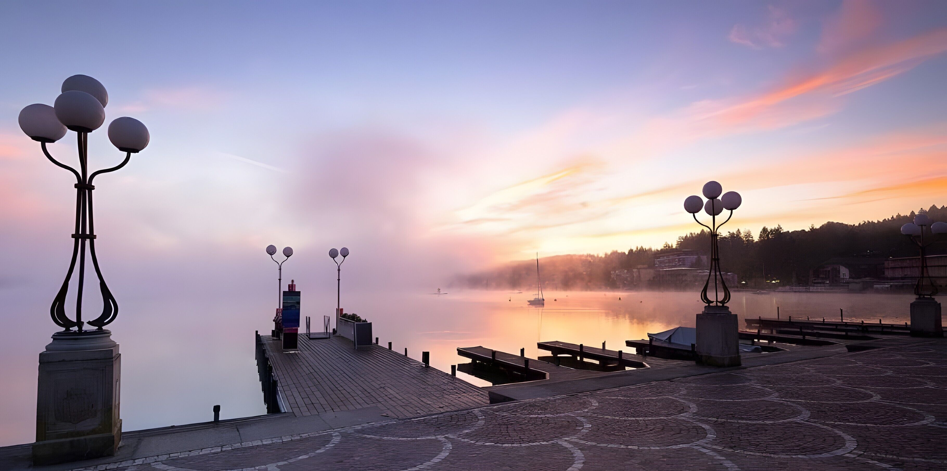A waterfront promenade with benches, lamp posts, and a calm body of water.